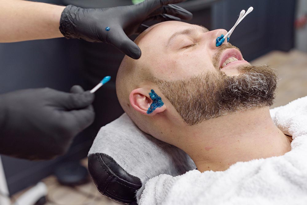 A man is undergoing wax hair removal for his nose and ear hair