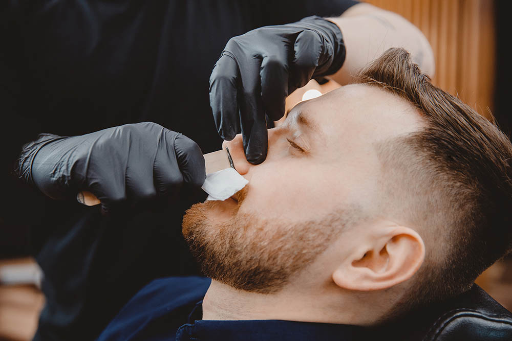 In a barbershop, a man is having his nose hair removed with wax
